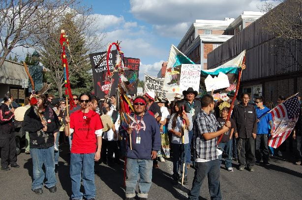 Indigenous people march and hold signs in the street to demonstrate their rights against colonization.