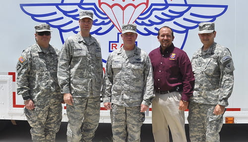 Four men in military uniforms stand with another man wearing a maroon button down.