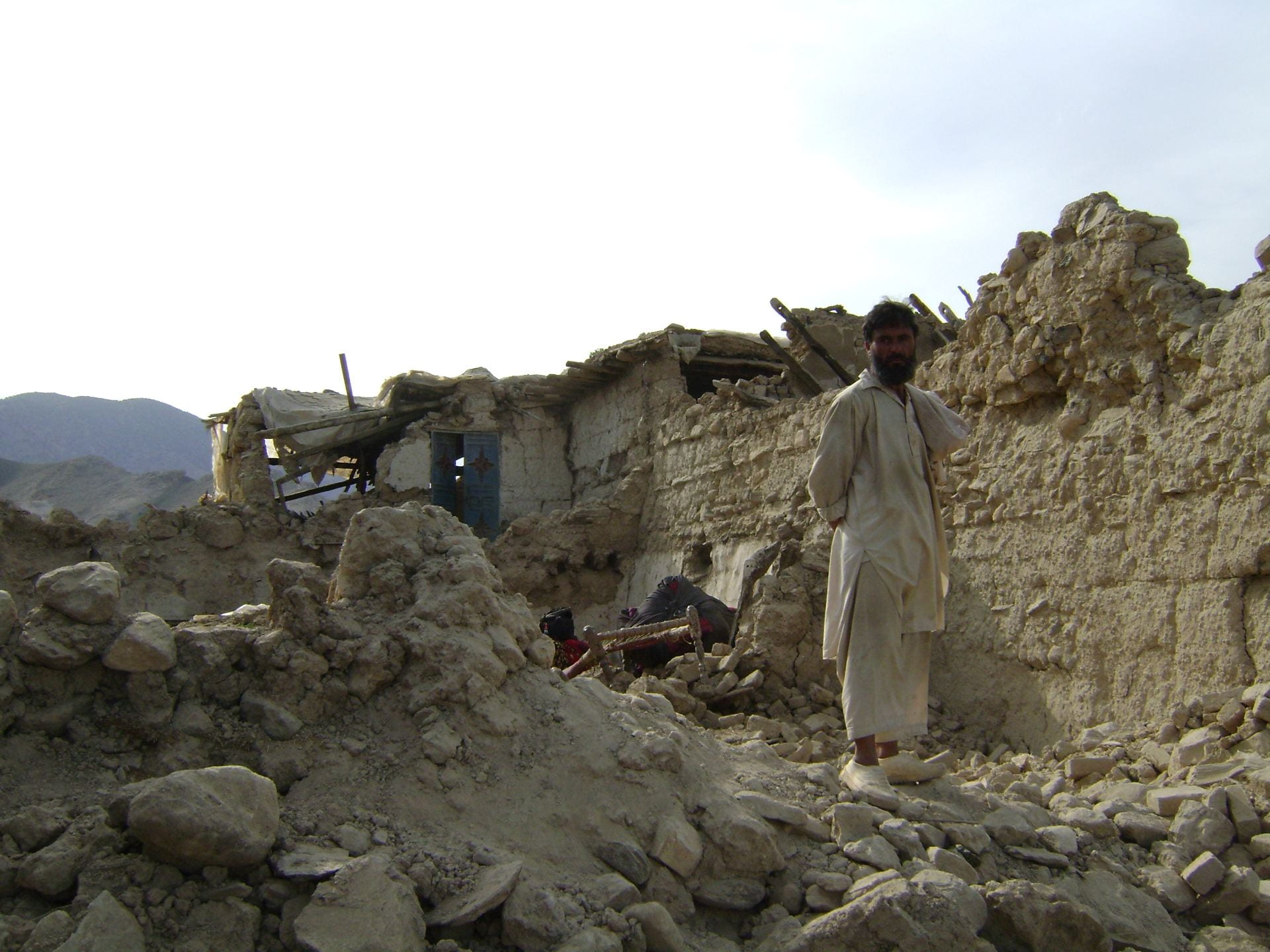 Image 1. Afghan Man standing in the rumble caused by an earthquake. Source: Flickr