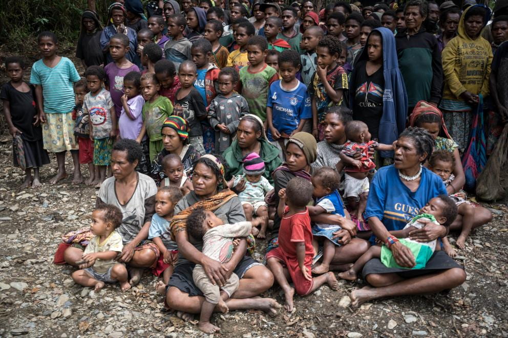 A group of West Papuan children, women, and men standing and sitting outside.