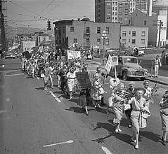 A black and white photo shows individuals marching in a protest against the construction of a highway.