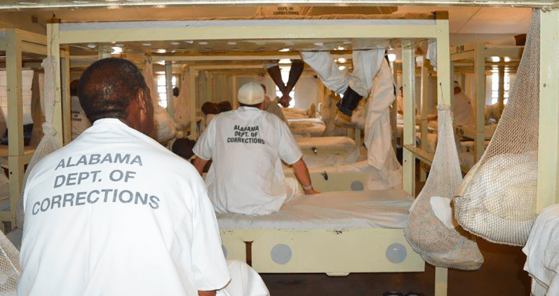 Inmates sitting on bunks wearing white jumpsuits
